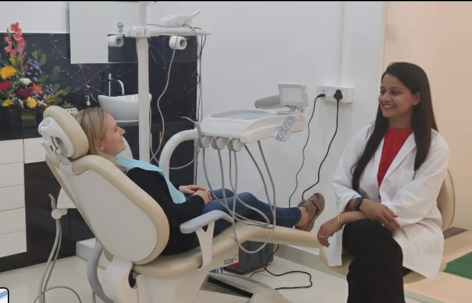 A visiting patient seated in the dental chair, talking with a doctor in a white coat beside her.