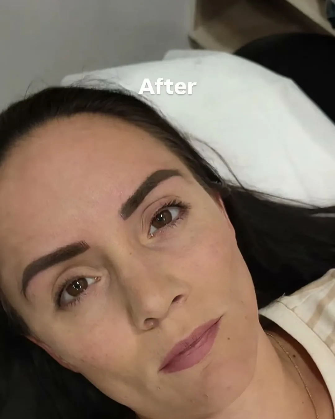 Close-up of a client's face after eyebrow microblading, lying on a treatment couch, with the word After printed on the frame.