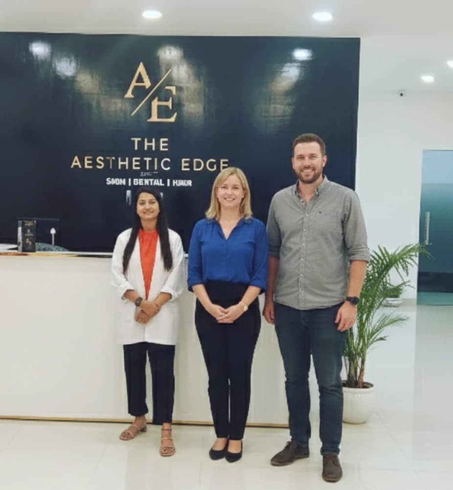 Two visitors from abroad standing with a clinician at The Aesthetic Edge reception, under the clinic's signage.