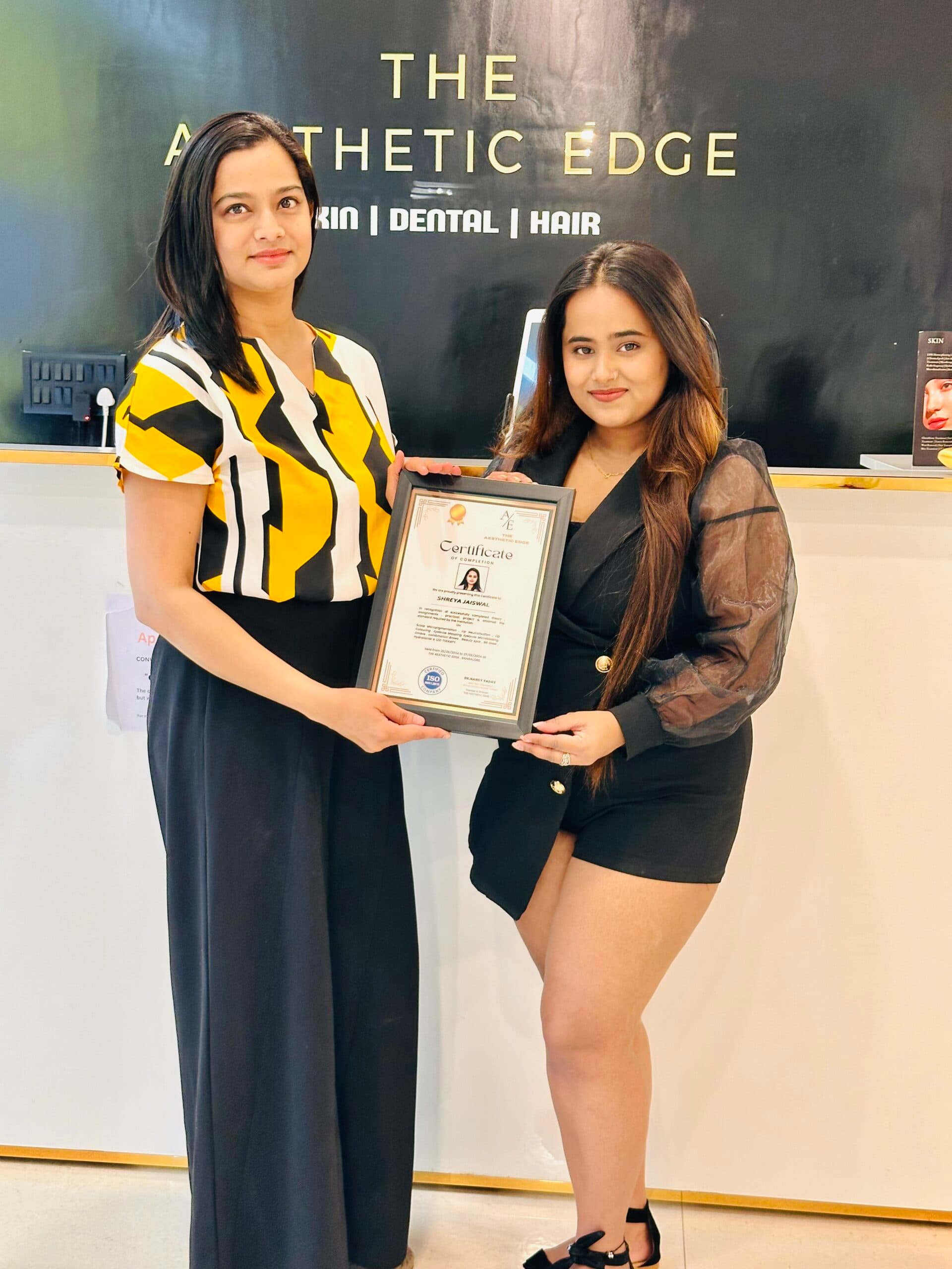 An academy graduate holding her framed Aesthetic Edge certificate of completion at the clinic reception